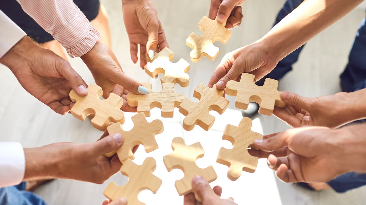 Viele Hände bilden einen Kreis und halten Puzzleteile in die Mitte