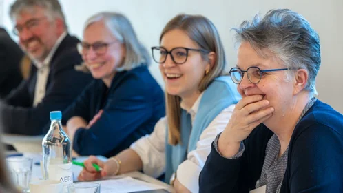 Lachende Teilnehmende der TH Bingen nebeneinander sitzend am Tisch