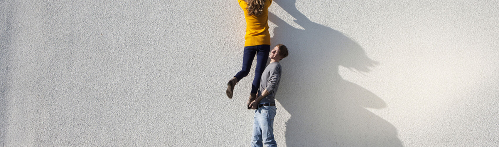 Mann hilft Frau beim Übersteigen einer Mauer