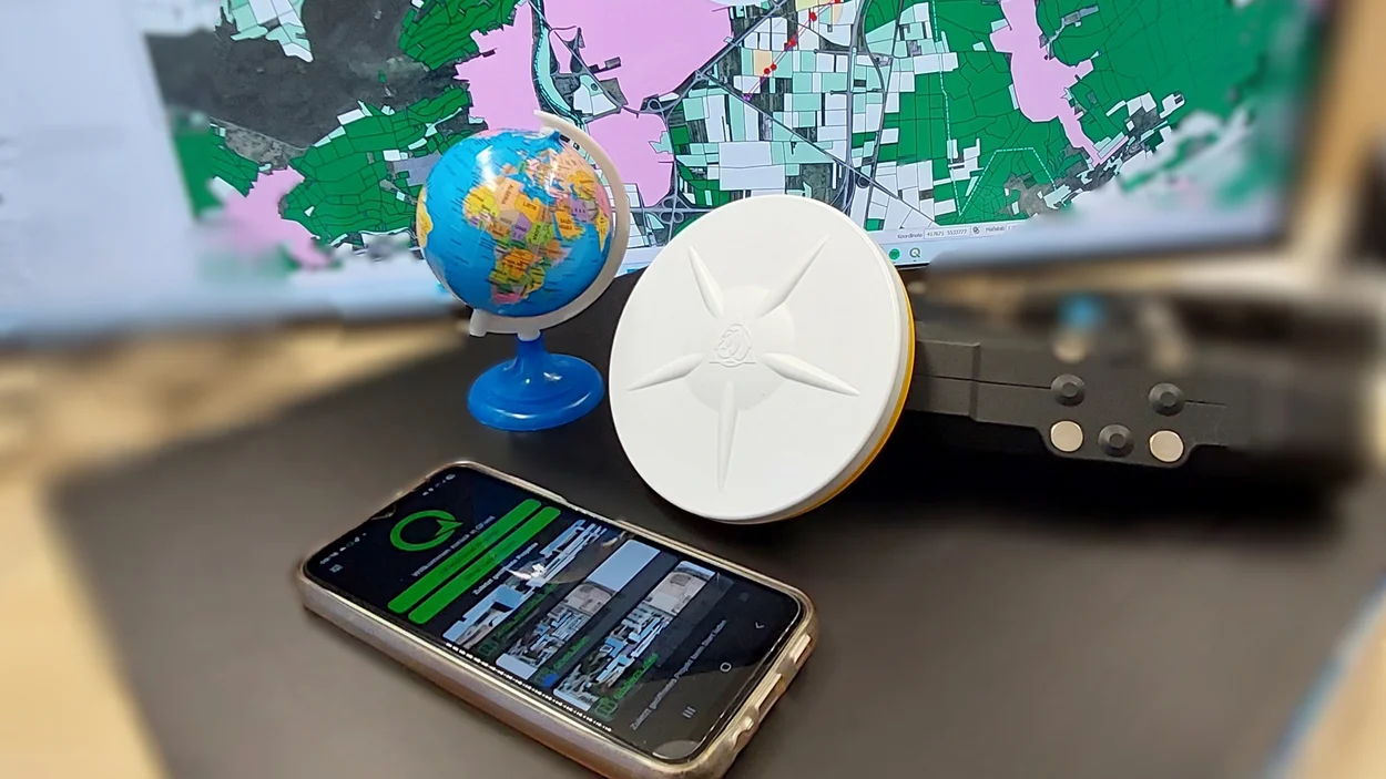 GNSS-Empfänger und ein Smartphone vor einer Weltkarte.