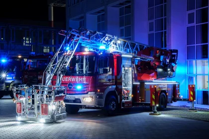 Beleuchtetes Feuerwehrauto mit langer Leiter und Blaulicht vor blau angestrahltem Gebäude