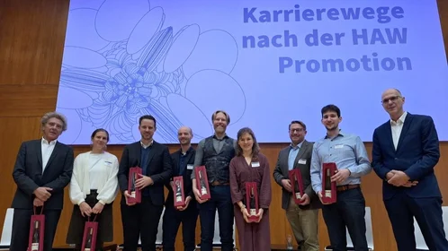 Menschen stehen in einer Reihe vor einer Leinwand, auf der "Karrierewege nach der HAW-Promotion" steht