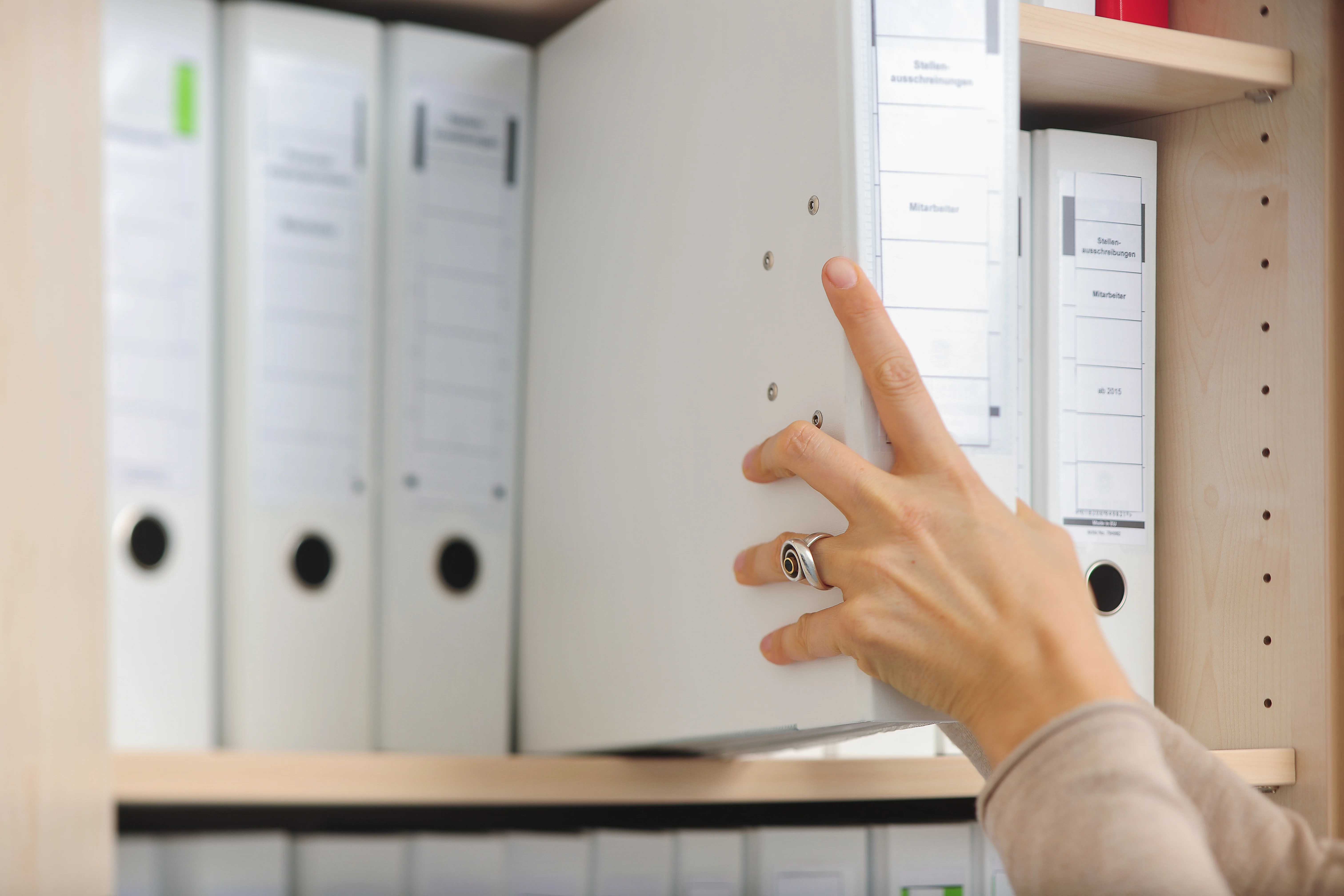 Das Bild zeigt eine Hand, die einen Ordner aus einem Regal nimmt.