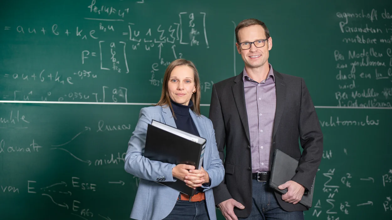 Zwei Profs vor einer Lehrtafel mit mathematischen Zeichen