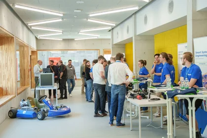 Menschen an Beratungsständen und kleines blaues Kartfahrzeug