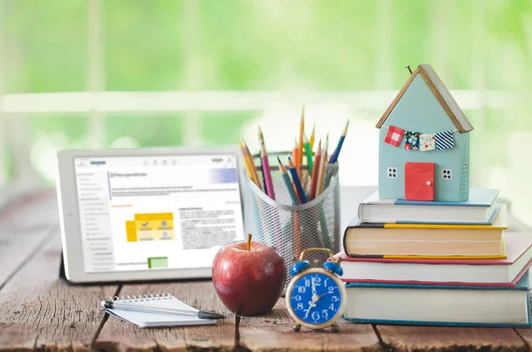 Schreibtisch mit Tablet, Bücherstapel, Wecker und Apfel