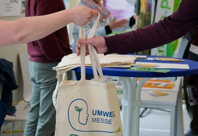 Eine Hand reicht einer anderen einen Stoffbeutel der Umweltmesse