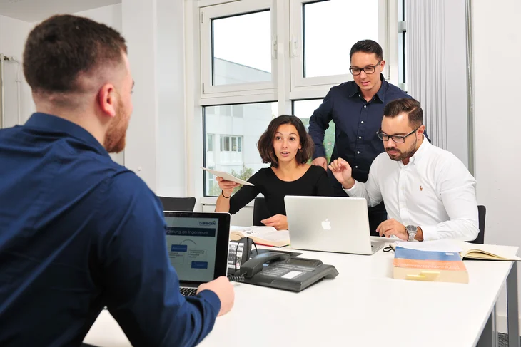 Hochschulangehörige arbeiten zusammen an ihrem Rechnern in einem Meeting-Raum