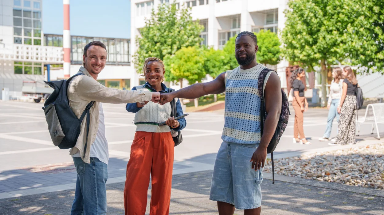 Weißer Student, schwarze Studentin und schwarzer Student machen "Fist Bump" und lachen in die Kamera