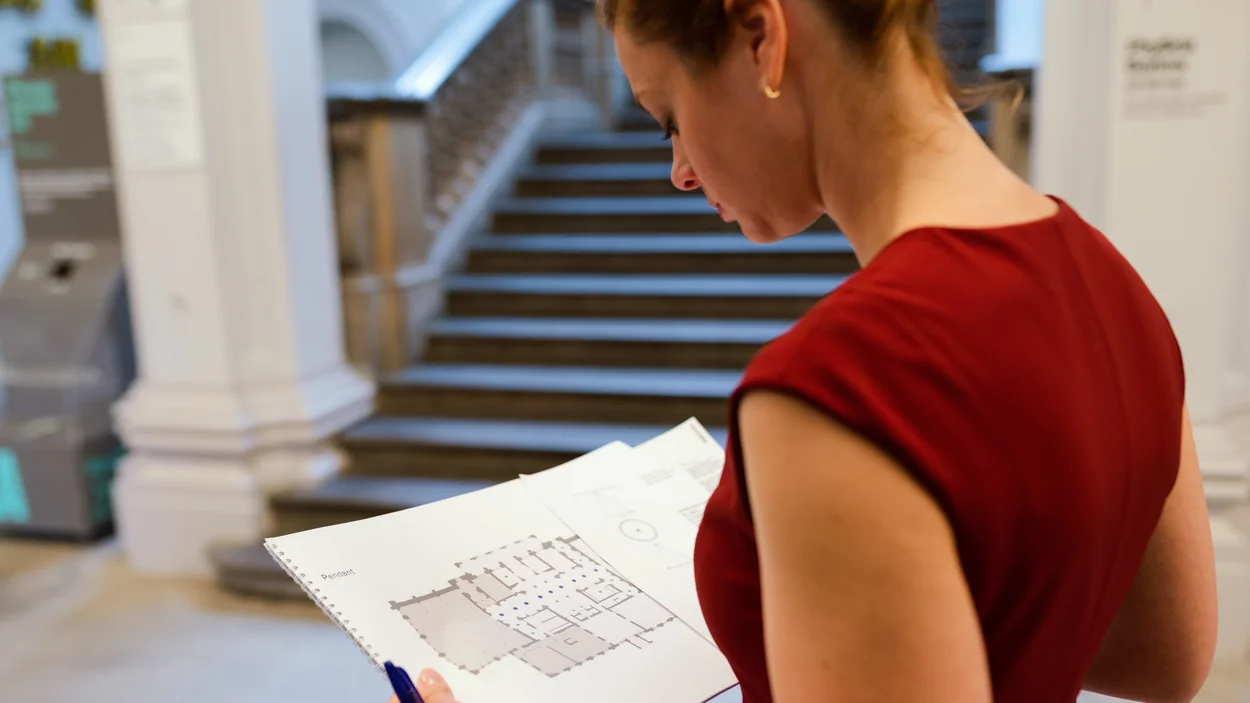 Frau in Halle mit Stufen blickt auf Plan