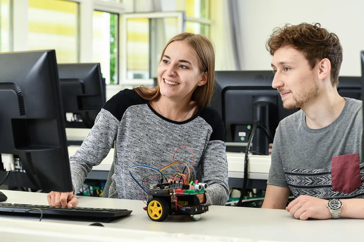 Studentin und Student zeigen lachend auf Computer