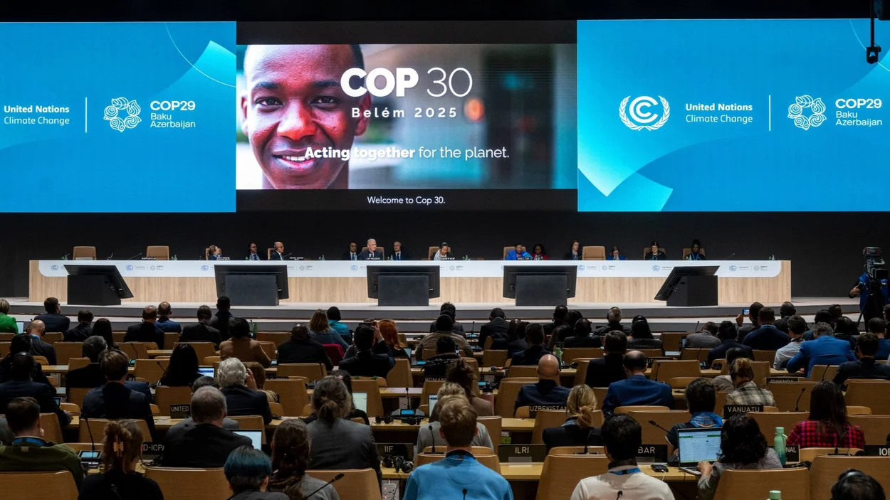 Menschen vor großer Präsentation mit dem Ausblick auf ein Gesicht einer schwarzen Person und dem Logo COP 30