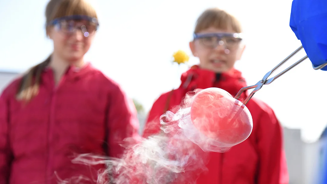 Das Bild zeigt ein Experiment während der Kinderhochschule und zwei Kinder im Hintegrund.