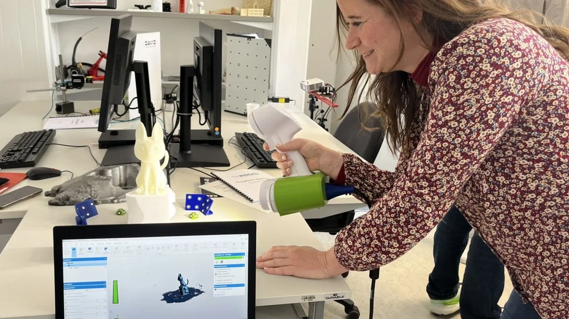 Junge Frau scannt ein Katzenmodell, das im Vordergrund auf dem Bildschirm als 3D-Modell eingeblendet wird