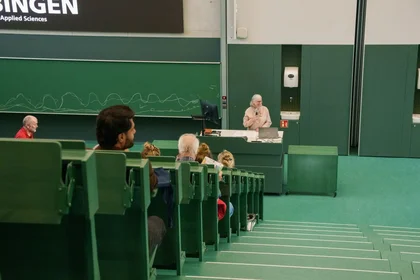 Blick entlang der Treppen in den grünen Hörsaal auf die lachende Präsidentin