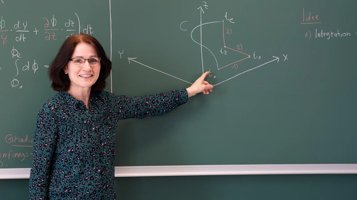 Dr. Helga Nutz zeigt auf mathematische Formeln an einer Schultafel