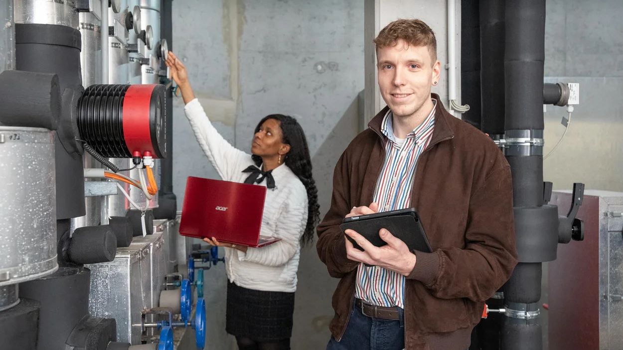 Ein Student im Vordergrund mit iPad, eine Studentin arbeitet weiter hinten an den Installationen
