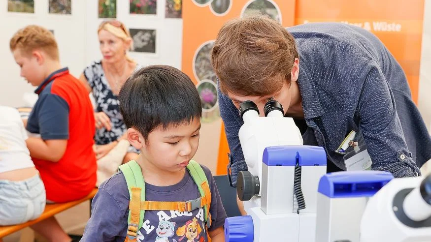 Kind steht mit Frau am Mikroskop