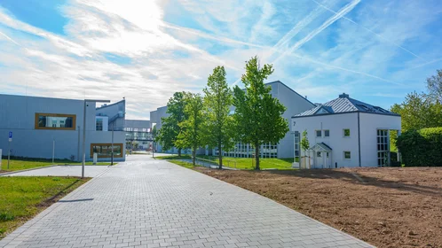 Helle, eckige Gebäude vor strahlend blauem Himmel, Weg geht zwischen den Gebäuden hindurch