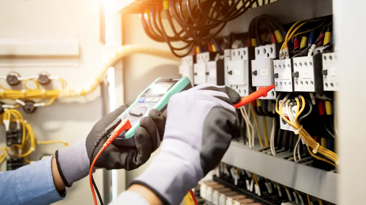 Elektroingenieur, der mit einem digitalen Multimeter die Stromspannung am Leistungsschalter und am Kabelverdrahtungssystem im Hauptstromverteilerkasten überprüft. 