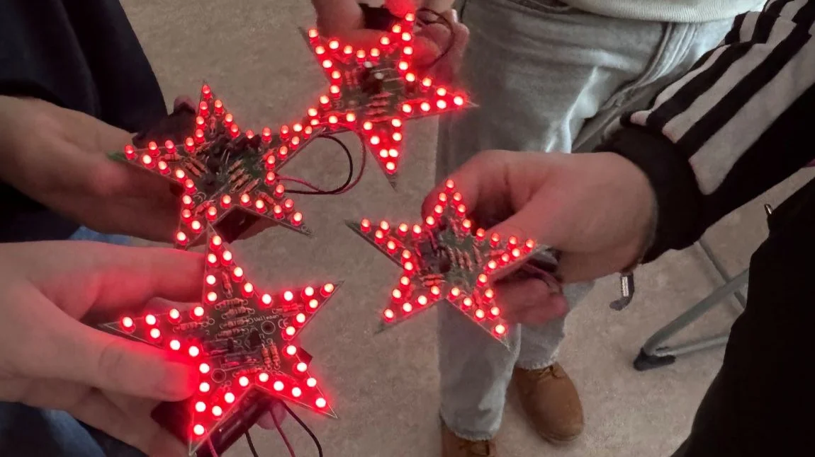 Vier Schüler*innen halten Sterne in die Mitte, deren Ränder mit roten Dioden leuchten