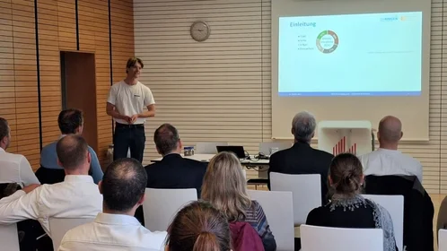 Junger Student steht vor einer Gruppe und präsentiert sein Forschungsprojekt